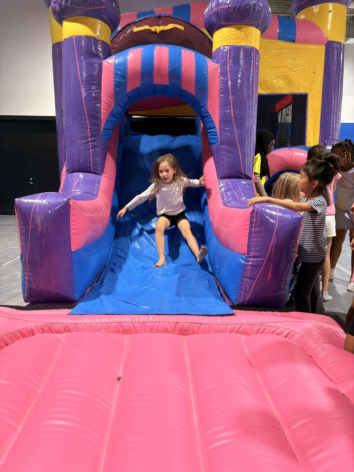 Child sliding joyfully on an inflatable play structure indoors at Laurus Summer Camp extended care program
